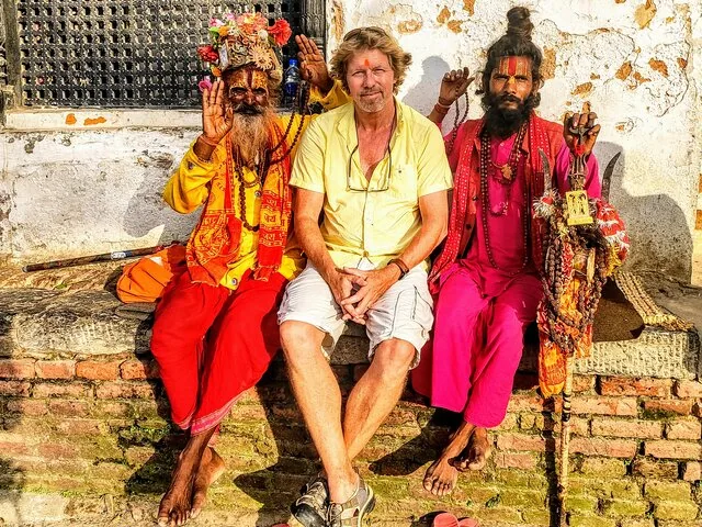 Un touriste pose assis entre deux sadhus.