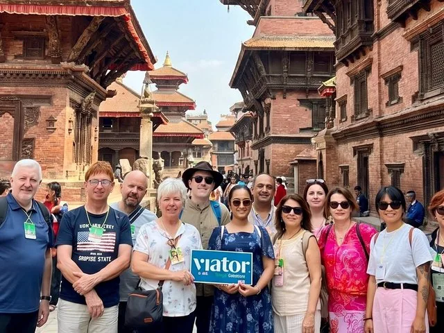 A group of tourists poses in a historic square holding a Viator sign.
