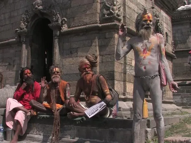 Plusieurs sadhus au visage et au corps peints se reposent près de structures en pierre.